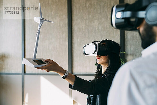 Geschäftsfrau mit VR-Brille untersucht Windturbinenmodell durch Kollegin im Büro