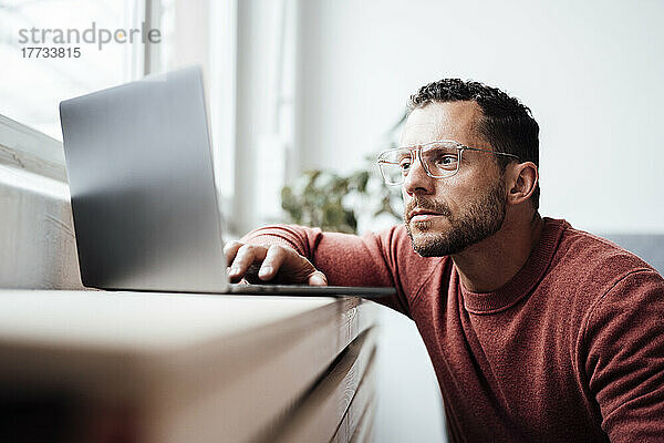 Freiberufler mit Brille arbeitet zu Hause am Laptop