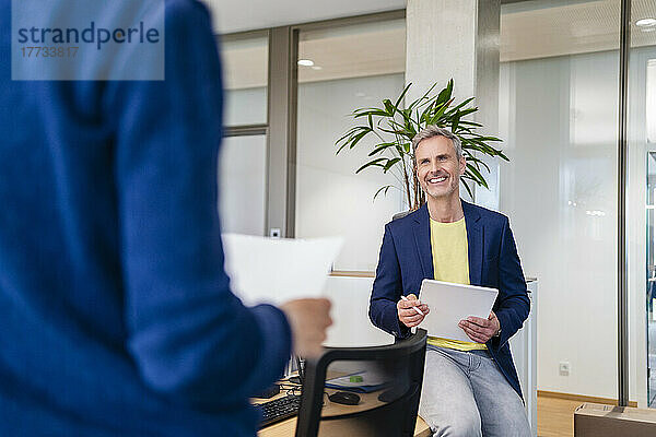 Lächelnder Geschäftsmann mit digitalem Tablet blickt Geschäftsfrau im Büro an