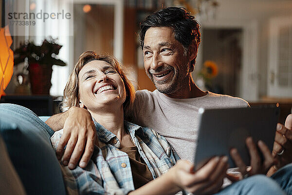 Glücklicher Mann und Frau mit Tablet-PC sitzen zu Hause