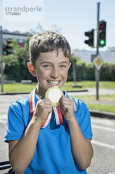 Lächelnder Junge zeigt an einem sonnigen Tag eine goldene Medaille