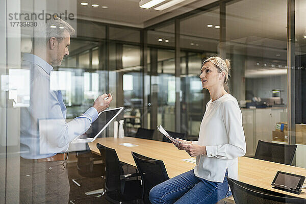 Geschäftsmann und Geschäftsfrau mit digitalem Tablet und Dokumenten unterhalten sich im Büro