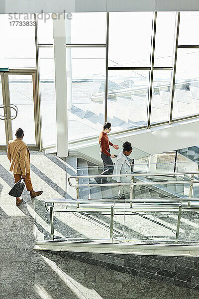Businessmen and businesswoman moving down on steps in modern office