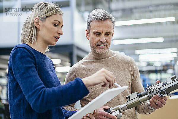 Geschäftsmann mit Gerät und Geschäftsfrau mit digitalem Tablet unterhalten sich in der Fabrik