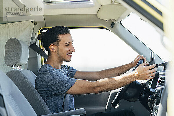 Lächelnder  gutaussehender Mann  der im Lieferwagen ein Smartphone benutzt