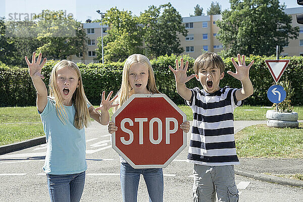 Girl holding stop sign board standing by friends on sunny day