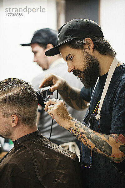 Junger Friseur schneidet einem Kunden im Salon mit einem Elektrorasierer die Haare