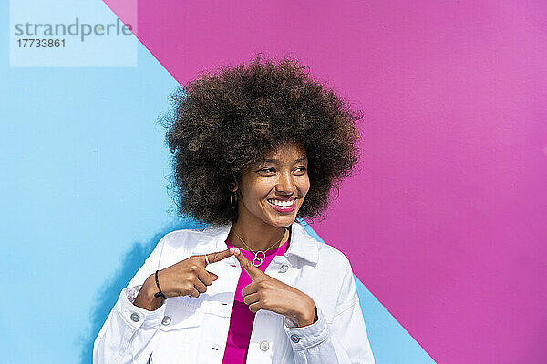 Glückliche Afro-Frau vor rosa und blauer Wand