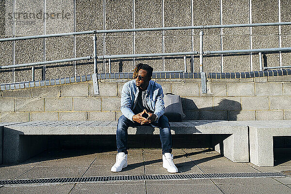 Junger Mann sitzt an einem sonnigen Tag auf einer Betonbank