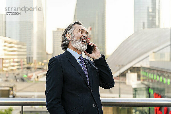 Fröhlicher Geschäftsmann mit grauem Haar  der auf dem Smartphone spricht