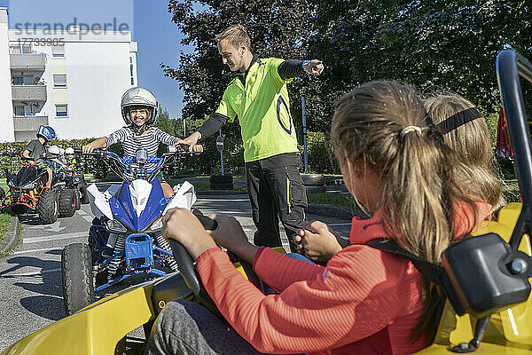 Junger Ausbilder unterstützt Jungen beim Quadfahren beim Verkehrserziehungstraining