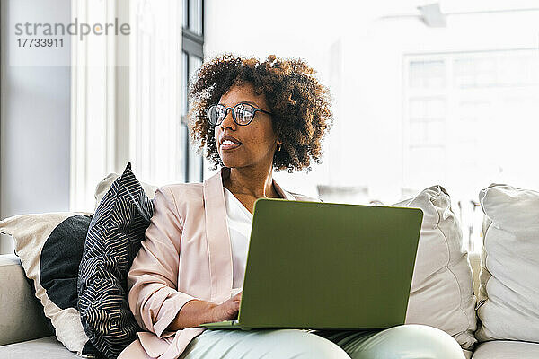 Junge Frau mit Laptop sitzt auf dem Sofa im Büro