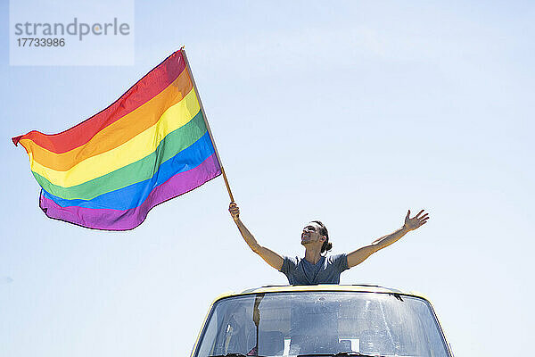 Lächelnder Mann mit Regenbogenfahne steht an einem sonnigen Tag im Lieferwagen
