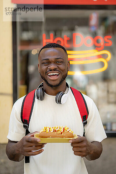 Glücklicher junger Mann hält Hot Dog