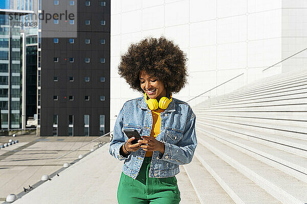 Lächelnde Afro-Frau  die an einem sonnigen Tag SMS über ihr Smartphone sendet