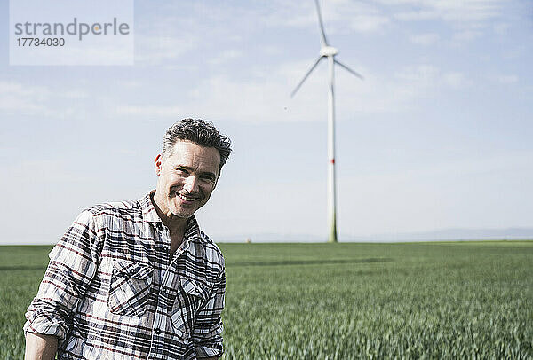 Glücklicher reifer Ingenieur  der an einem sonnigen Tag vor der Windkraftanlage steht