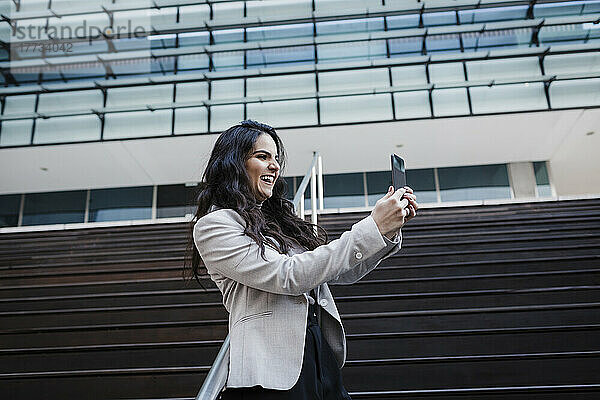 Glückliche Geschäftsfrau bei Videoanruf über Smartphone vor Bürogebäude