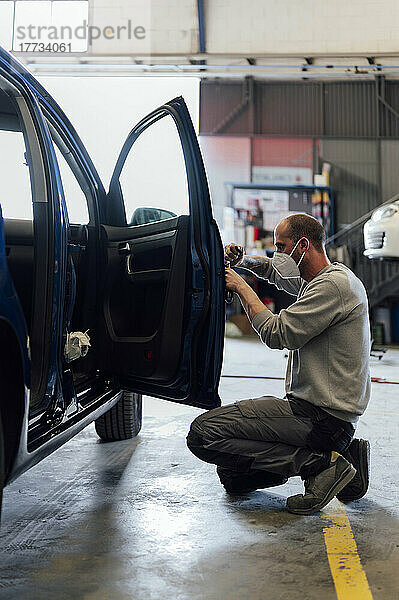 Automechaniker arbeitet in der Werkstatt an der Autotür