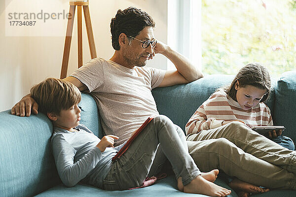 Reifer Mann sitzt mit Tochter und Sohn und nutzt Tablet-PC zu Hause
