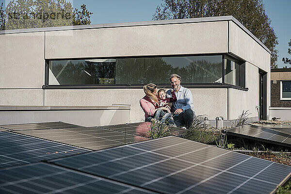 Glückliches Mädchen mit Eltern  die am Solarpanel auf dem Dach sitzen