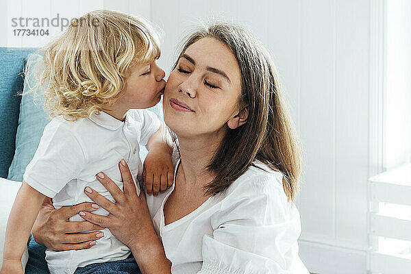 Cute boy kissing mother on cheek at home