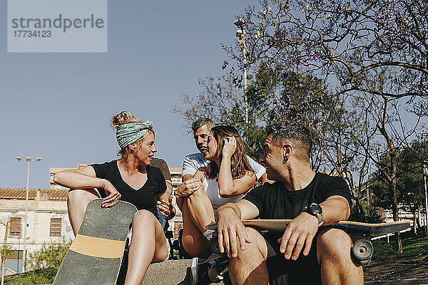 Freunde diskutieren miteinander und sitzen an einem sonnigen Tag im Skateboardpark