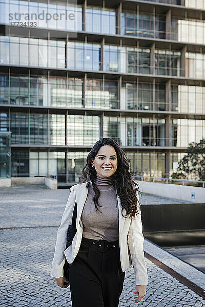 Lächelnde junge Geschäftsfrau  die vor einem modernen Bürogebäude läuft
