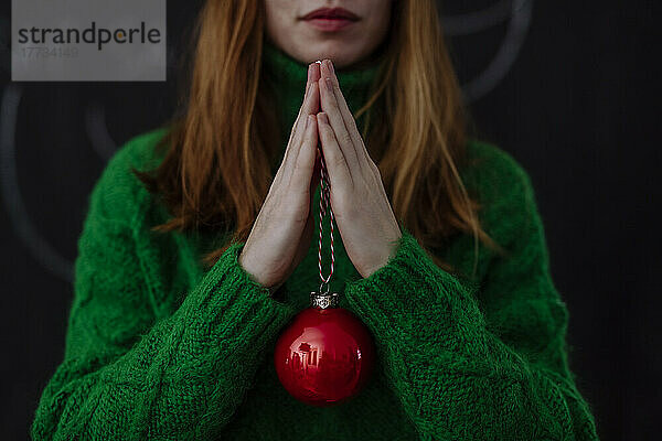 Frau mit roter Weihnachtskugel steht vor schwarzem Hintergrund