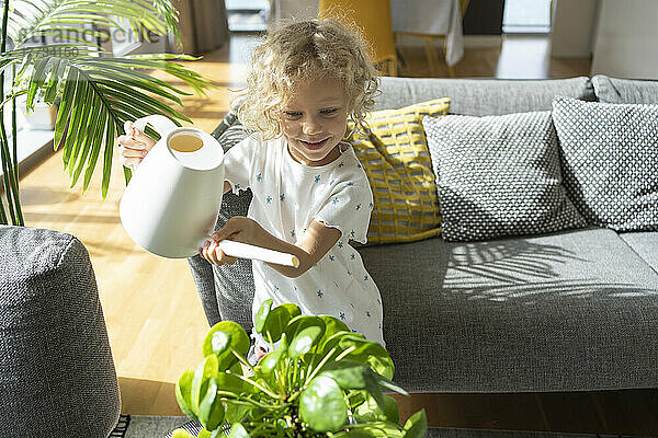 Girl watering plant in living room at home