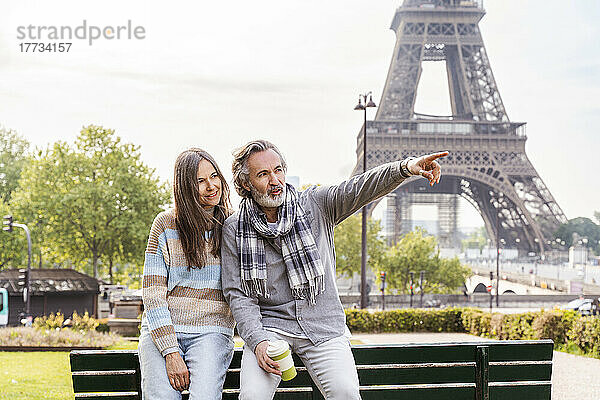 Reifer Mann zeigt weg und sitzt mit Freundin auf einer Bank im Park  Eiffelturm  Paris  Frankreich