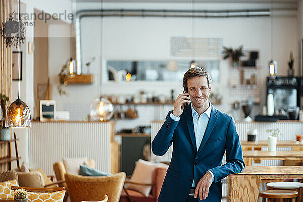 Glücklicher Freiberufler  der im Café mit dem Smartphone spricht