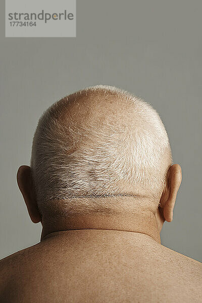 Oberkörperloser älterer Mann mit kurzen grauen Haaren vor grauem Hintergrund