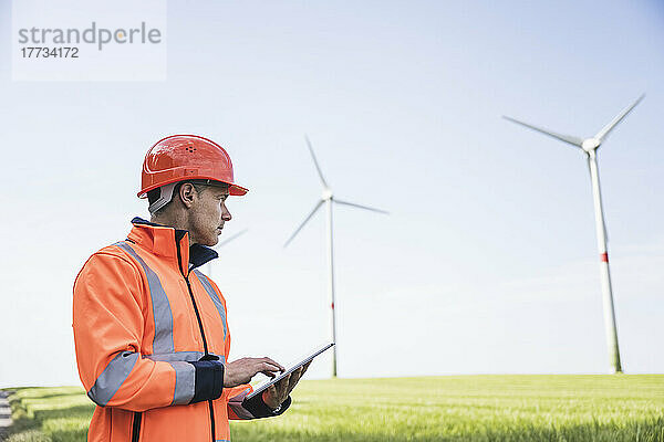 Ingenieur hält Tablet-PC an Feldwindkraftanlage