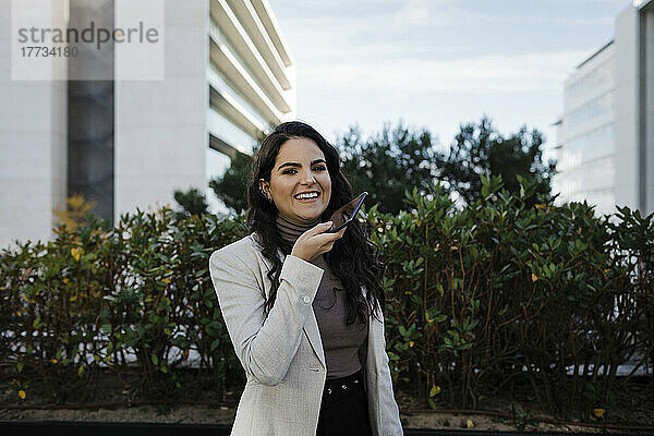 Lächelnde  schöne junge Geschäftsfrau  die im Finanzviertel über den Smartphone-Lautsprecher spricht