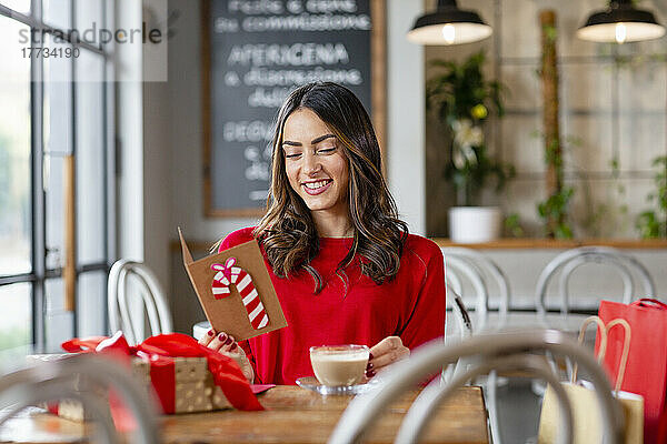 Glückliche schöne Frau liest Weihnachtskarte im Café sitzend