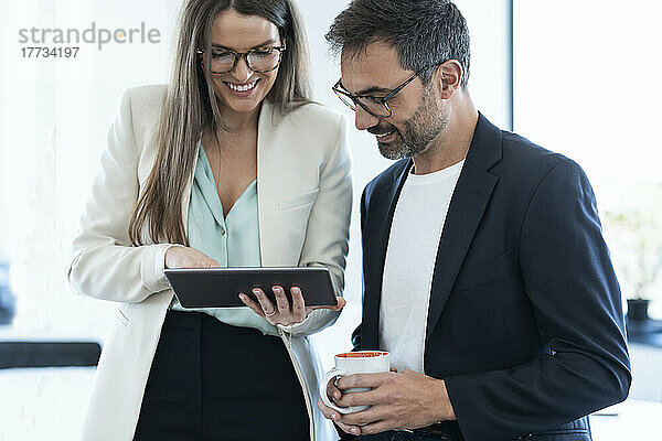 Lächelnde Geschäftsfrau diskutiert über Tablet-PC mit Geschäftsmann im Büro