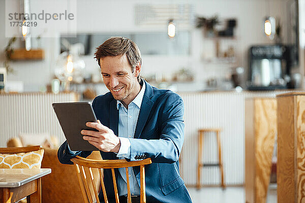 Glücklicher Geschäftsmann sitzt auf einem Stuhl und benutzt einen Tablet-PC im Café