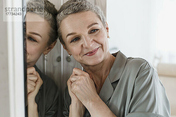 Porträt einer reifen Frau mit kurzen grauen Haaren  die sich an den Spiegel lehnt