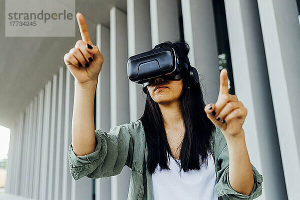 Young woman wearing virtual reality simulator pointing in front of column