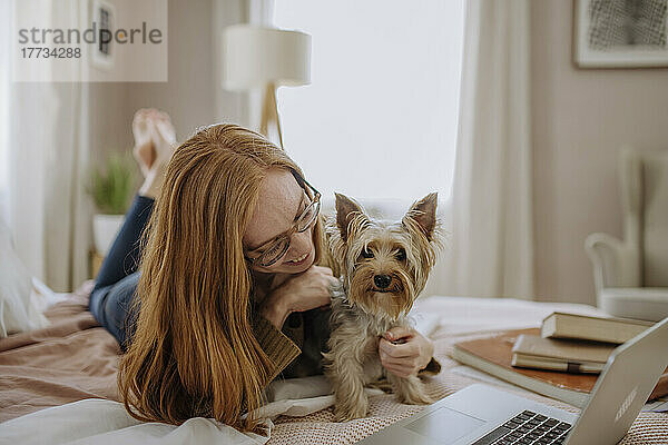 Lächelnde Frau spielt mit Hund  der zu Hause im Bett liegt