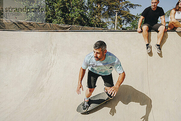 Mann fährt Skateboard auf Sportrampe mit Freunden im Hintergrund