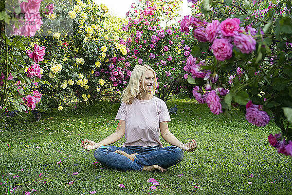 Lächelnde Frau praktiziert Yoga inmitten von Rosenpflanzen im Garten