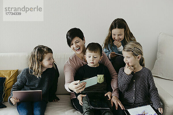 Glückliche Familie mit drahtloser Technologie  die zu Hause zusammen auf dem Sofa sitzt