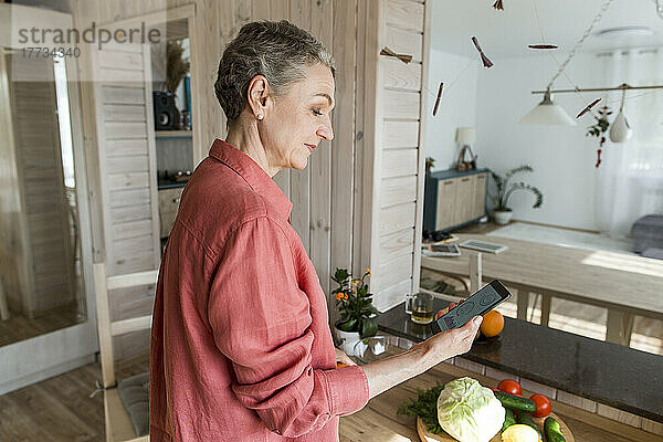 Frau in der Küche zu Hause hält Smartphone in der Hand