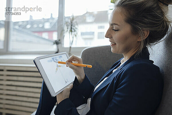 Lächelnde Geschäftsfrau zeichnet im Büro eine Windkraftanlage auf einem Tablet-PC