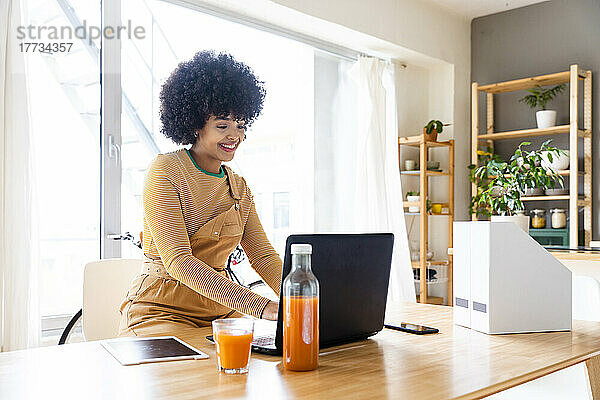 Lächelnde Frau benutzt Laptop am Tisch im Wohnzimmer