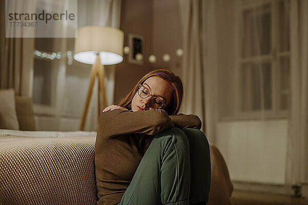 Einsame Frau mit geschlossenen Augen sitzt zu Hause vor dem Bett
