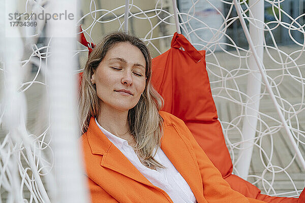 Woman resting with eyes closed on hanging chair