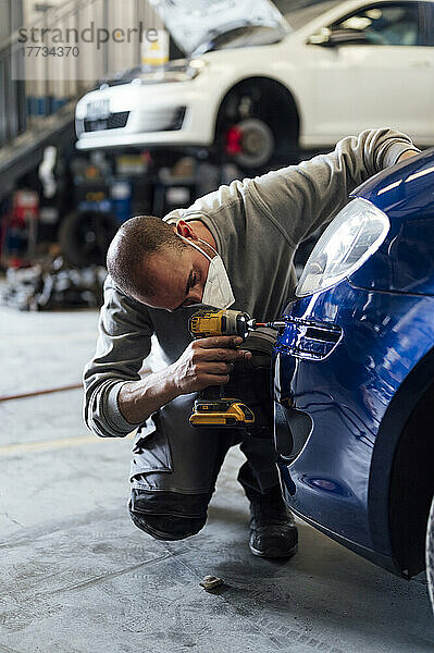 Automechaniker repariert Auto mit Elektroschrauber in der Werkstatt