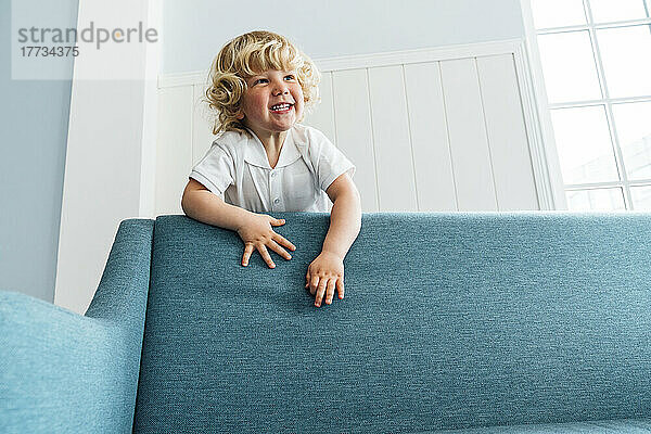 Cute boy climbing on sofa in living room at home
